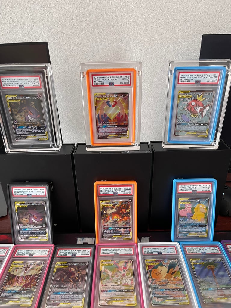 Collection of graded Pokemon trading cards displayed in protective cases and slabs with authentication labels, arranged on black stands and surface.